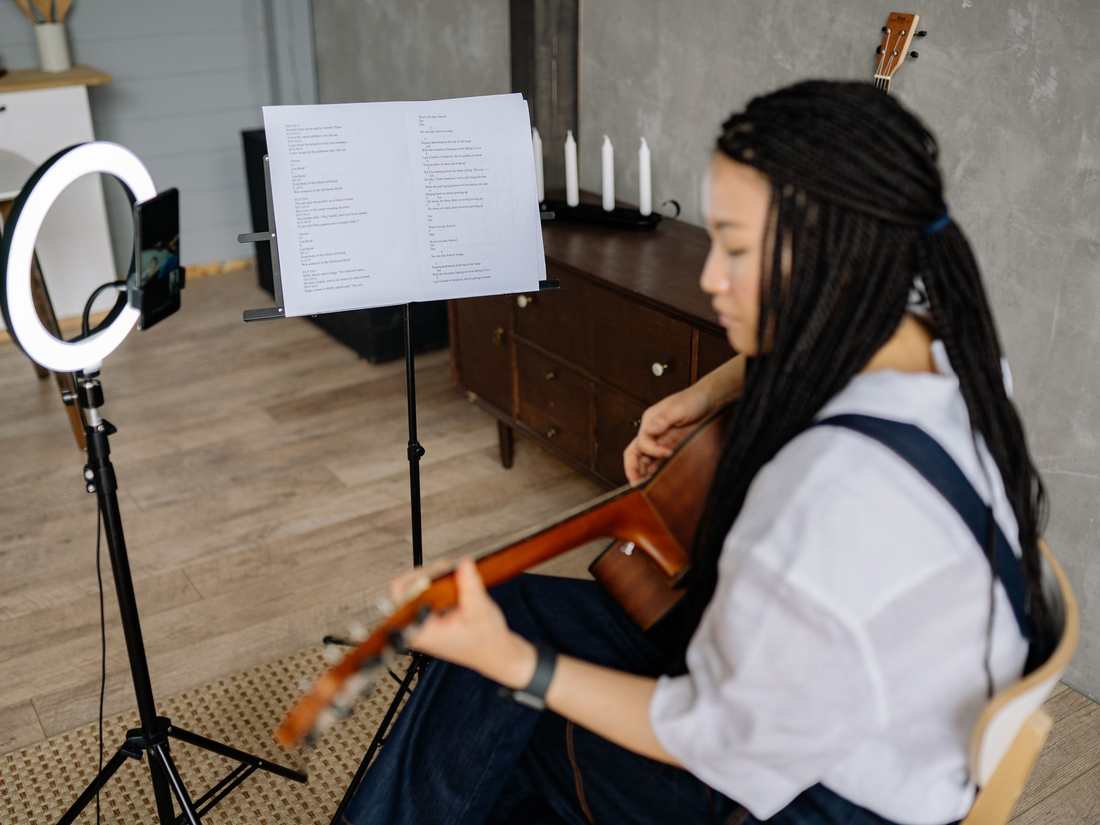 A guitarist recording herself at home, ring light and phone beside a music stand