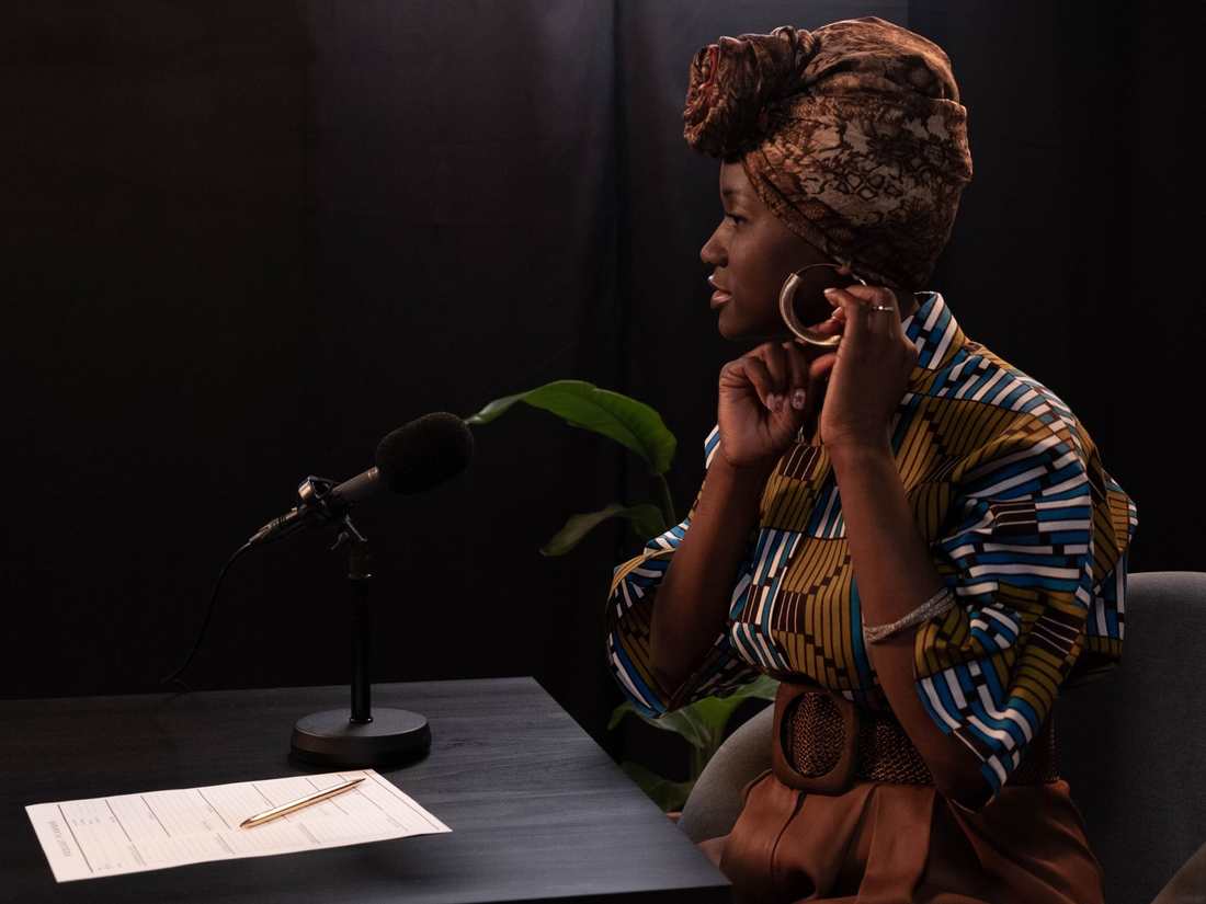 A woman speaking into a studio microphone, notes on the table beside her