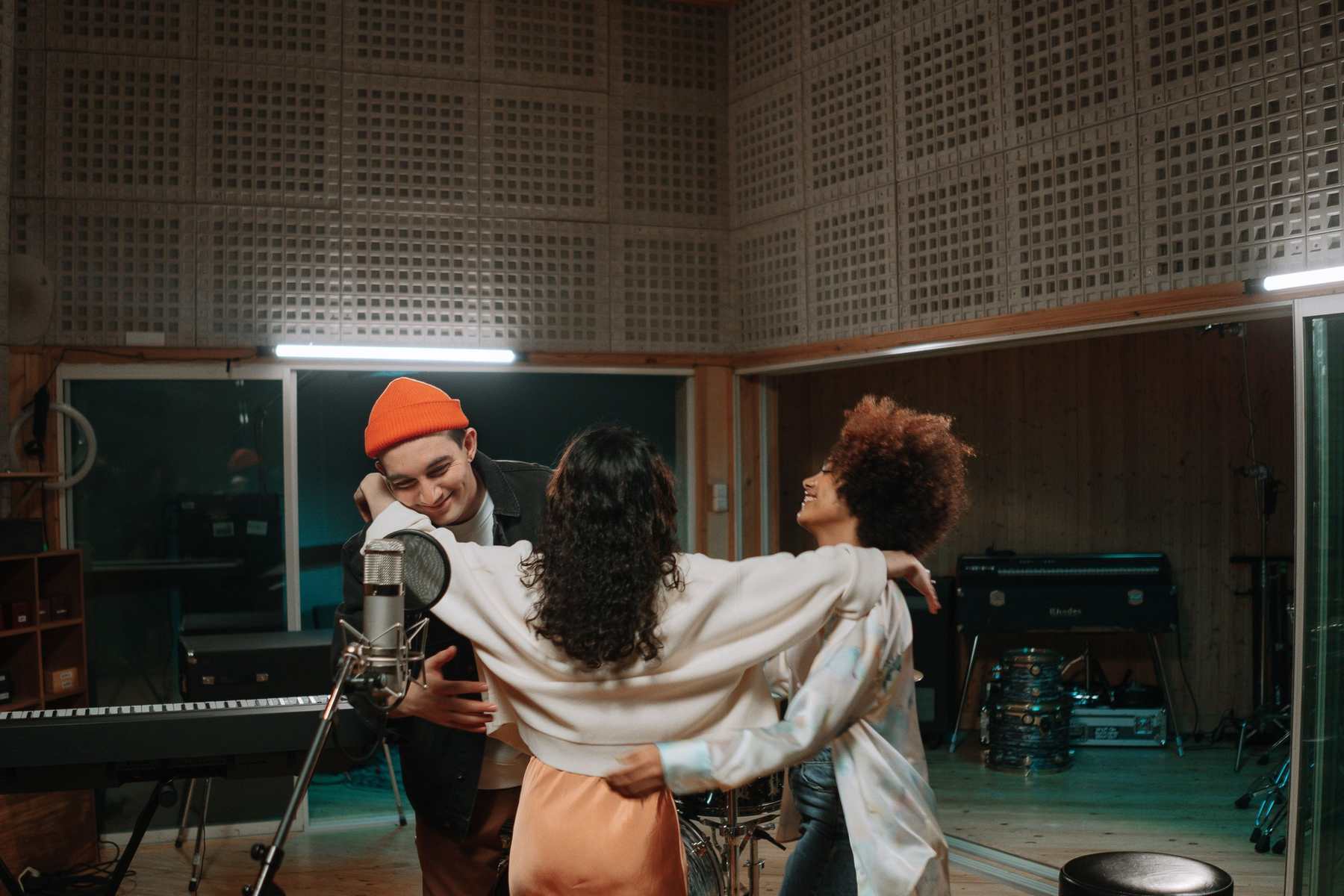 Three musicians together in a recording studio live room, arms around each other