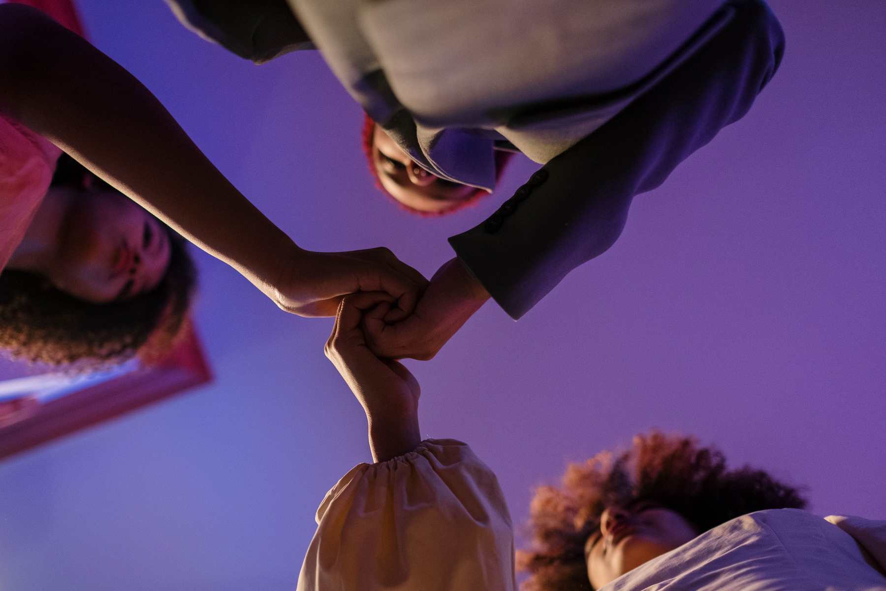 Four people gathered in a circle, hands joined in the centre, seen from below
