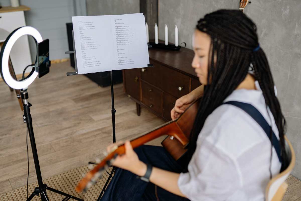 A guitarist recording herself at home, ring light and phone beside a music stand