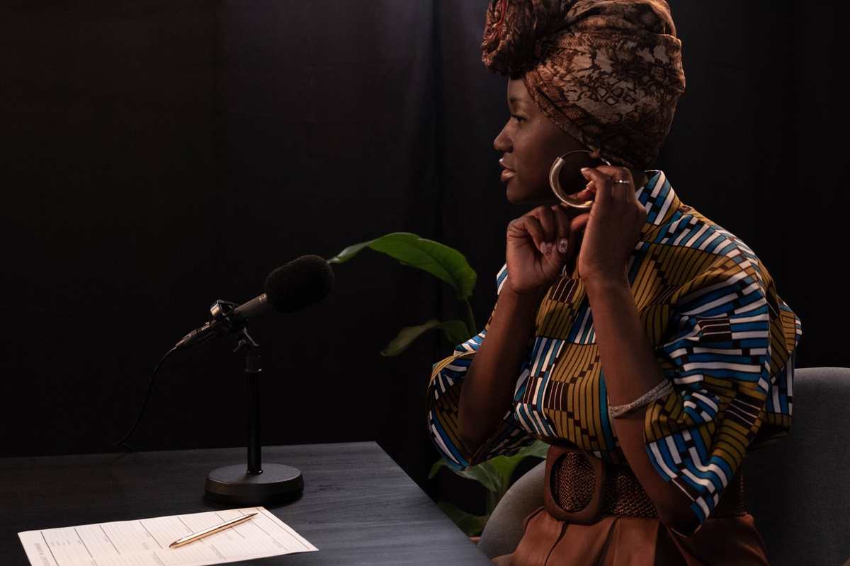 A woman speaking into a studio microphone, notes on the table beside her